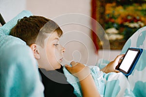 School kid boy reading an ebook at night. Adorable child in bed with interesting book. Portable reader holding by