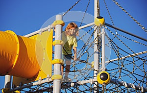 School kid climbing in the school playground. Cute and happy little child boy climbed on top of the rope web, kids