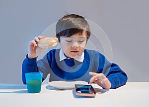 School kid eating homemade burger and typing on mobile phone, Hungry boy eating homemade bread sandwiches for his lunch, Child