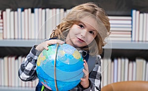 School kid pupil looking at globe in library at the elementary school. World globe. School kid 7-8 years old with book