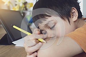 School kid in self isolation using tablet for homework,Tried child closing eyes lying head down lon his arms, Boy stay at home