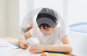 School kid using colour pen drawing or writing the letter on paper, Young boy doing homework, Child with pen writing notes in