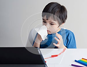 School kid wiping nose with tissue and watching cartoon on tablet,Child stay at home during corona virus home quarantine,E-