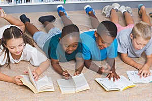 School kids lying on floor reading book in library