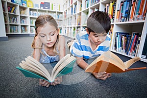 School kids lying on floor and reading a book in library