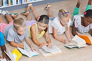 School kids lying on floor reading book in library