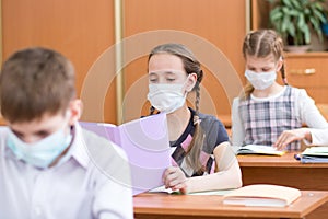 School kids with protection mask against flu virus at lesson in classroom