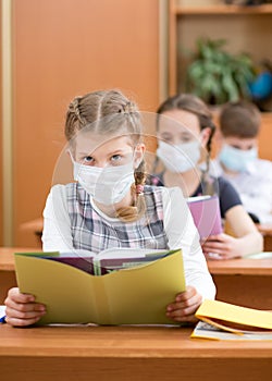 School kids with protection mask against flu virus at lesson in classroom