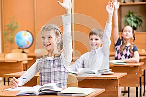 School kids with raised hands at lesson in classroom