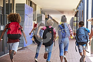 School kids running in elementary school hallway, back view