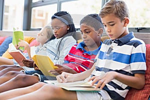 School kids sitting on sofa and reading book in library