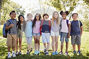 School kids stand embracing in a row outdoors, full length