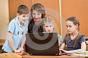 School kids and teacher using laptop at lesson