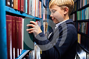 school life. caucasian kid boy is searching and choosing book in bookshop