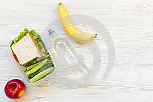 School lunch box with sandwich, fruits and bottle of water on white wooden background, top view. From above.