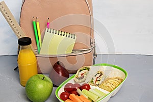 School lunch box with sandwich, vegetables, water, fruits, backpack with school objects