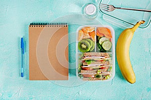 School lunch box with sandwich, vegetables, water, and fruits on table.