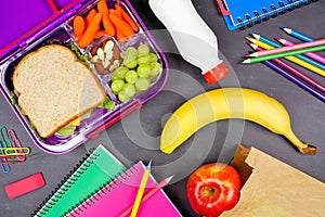 School lunch box and school supplies, overhead on a chalkboard background