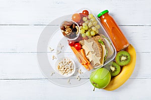 School lunch box with vegetables, fruits and sandwich for healthy snack on white wooden table top view.