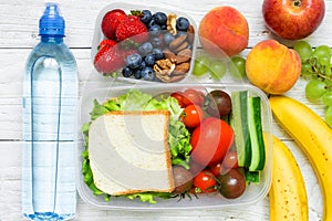 School lunch boxes with sandwich, fresh fruits and vegetables, berries and nuts and bottle of water