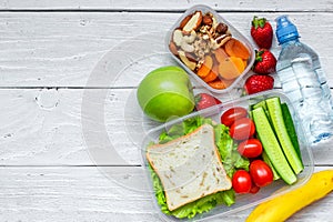 School lunch boxes with sandwich and fresh vegetables, bottle of water, nuts and fruits