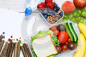 School lunch boxes with sandwich, fruits, vegetables and bottle of water with colored pencils