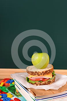 School lunch, sandwich and apple on classroom desk with blackboard, copy space, vertical