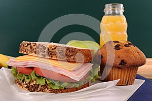 School lunch sandwich, cake and drink on classroom desk with blackboard