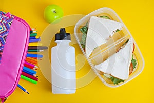 School lunch sandwich and green apple, bottle of water, healthy eating concept, colorfu encils yellow background, top view with co