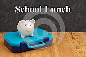 School lunchbox with a piggy bank on wood desk with a chalkboard photo