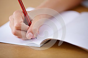 School, notebook and hand of child writing on desk with pencil, notes and learning for education. Paper, closeup and