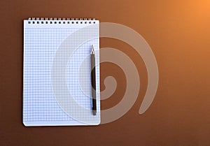 School notebook with pen on a brown table top view, office desktop, office supplies on a brown background. copy space