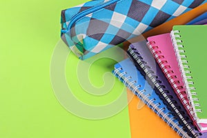 School notebooks of different colors and a pencil case on a bright orange and green background. School supplies.
