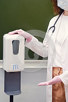 School nurse showing automatic sanitizer dispenser in class. Learning difficulties in the flu pandemic