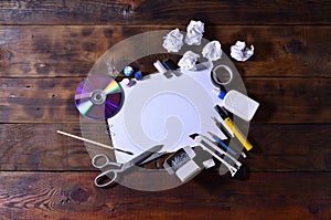 A school or office still life with a white blank sheet of paper and many office supplies. The school supplies lie on a brown wood