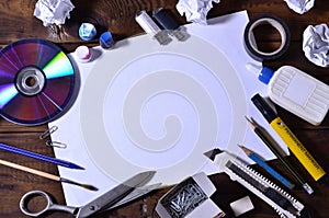 A school or office still life with a white blank sheet of paper and many office supplies. The school supplies lie on a brown wood