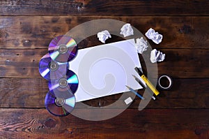 A school or office still life with a white blank sheet of paper and many office supplies. The school supplies lie on a brown wood