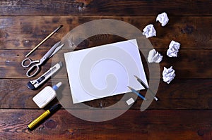 A school or office still life with a white blank sheet of paper and many office supplies. The school supplies lie on a brown wood