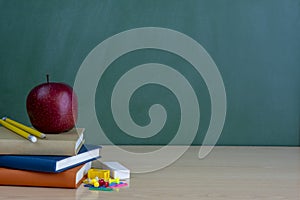 School and office supplies on classroom table in front of blackboard.