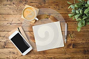 School paper with coffee cup, smartphone and plant on wooden table. Top view from above