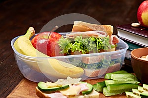 School or picnic lunch box with sandwich and various colorful vegetables and fruits on wooden background, close up.