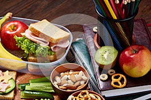 School or picnic lunch box with sandwich and various colorful vegetables and fruits on wooden background, close up.