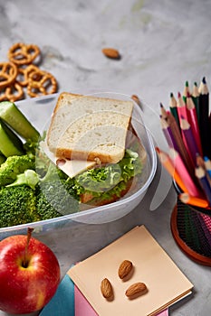 School or picnic lunch box with sandwich and various colorful vegetables and fruits on wooden background, close up.