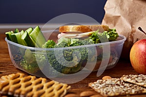 School or picnic lunch box with sandwich, various vegetables, fruits and cookies on wooden background, close up.