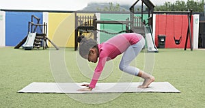 In a school playground, a young Hispanic girl practices yoga