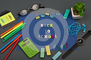 School set with blue paper, text `Back to school` of wooden letters, calculator, markers, eyeglasses, watch