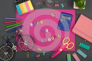 School set with pink paper, text `Back to school` of wooden letters, bicycle model, calculator, crayons, scissors,