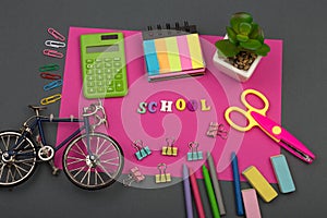 School set with pink paper, text `School` of wooden letters, bicycle model, calculator, crayons, scissors, note pad