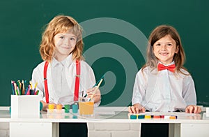 School smiling children girl and boy painting with paints color and brush in classroom on school blackboard background