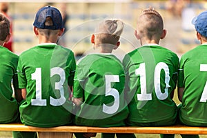 School soccer players sitting on a wooden substitute bench. Group of children boys playing sports competition game